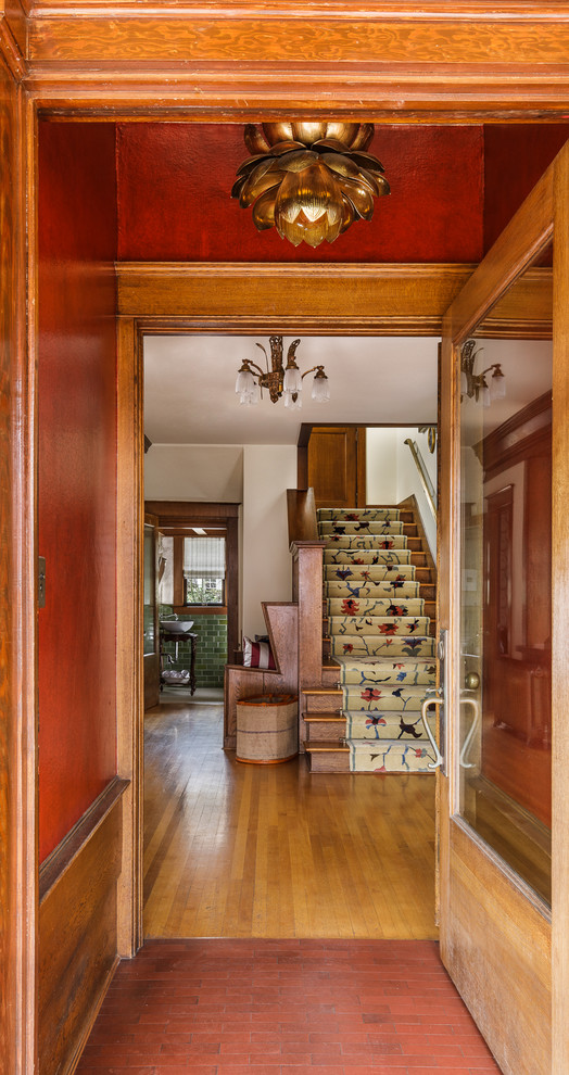 ポートランドにあるお手頃価格の小さなトラディショナルスタイルのおしゃれな玄関ロビー (赤い壁、淡色無垢フローリング、淡色木目調のドア、茶色い床) の写真