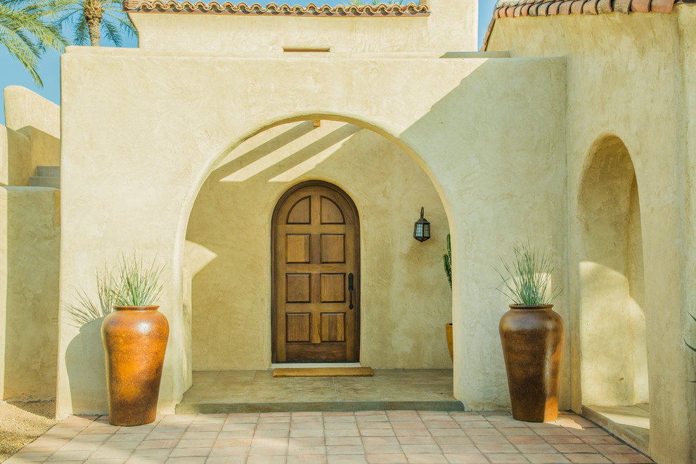 フェニックスにあるラグジュアリーな巨大なサンタフェスタイルのおしゃれな玄関ドア (ベージュの壁、コンクリートの床、木目調のドア、グレーの床) の写真