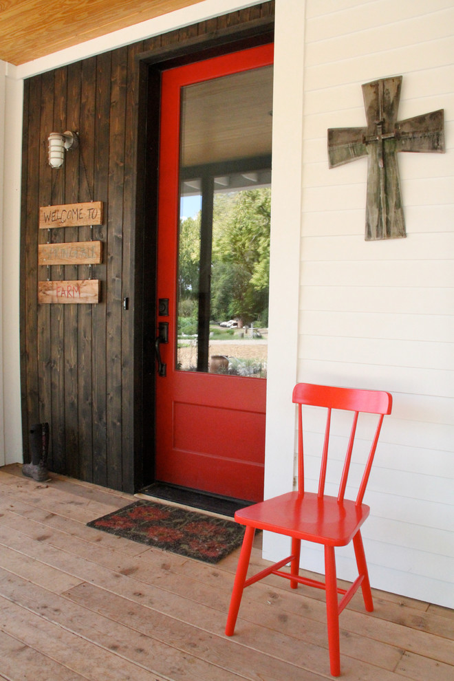 This is an example of a medium sized country front door in Austin with a single front door, a red front door, white walls and medium hardwood flooring.