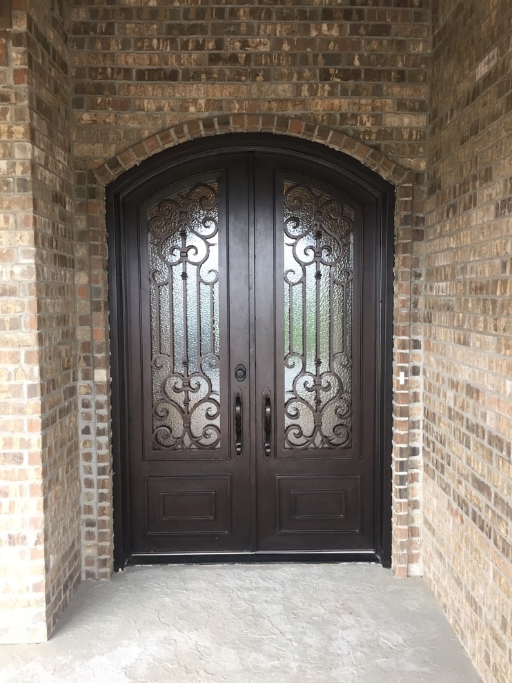 Modelo de puerta principal rústica grande con puerta doble, paredes beige, suelo de cemento y puerta de madera oscura