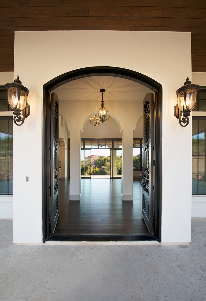Modelo de puerta principal mediterránea grande con paredes blancas, suelo de madera oscura, puerta doble y puerta metalizada
