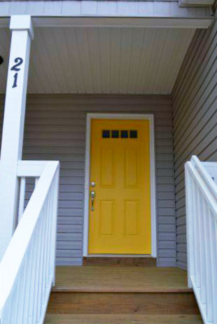 Ispirazione per una porta d'ingresso minimal di medie dimensioni con pareti grigie, pavimento in legno massello medio, una porta a pivot e una porta gialla