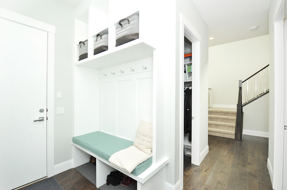 Cette image montre un petit hall d'entrée minimaliste avec un mur gris, parquet foncé, une porte simple, une porte blanche et un sol marron.