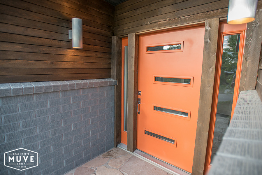 Exempel på en stor modern ingång och ytterdörr, med grå väggar, betonggolv, en pivotdörr och en orange dörr