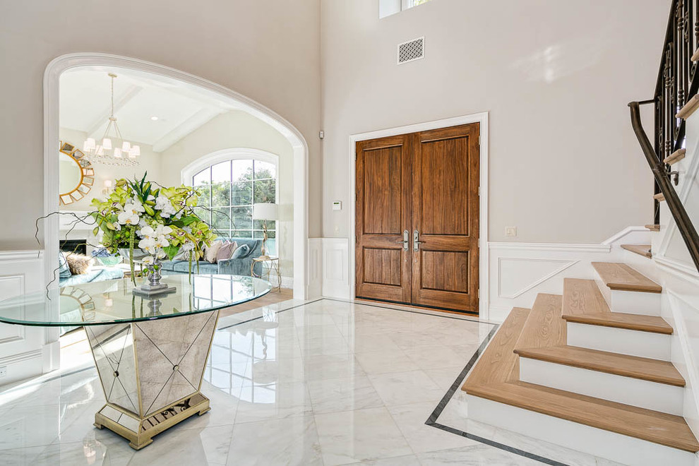 ロサンゼルスにある高級な広いトランジショナルスタイルのおしゃれな玄関ドア (グレーの壁、大理石の床、木目調のドア、白い床) の写真