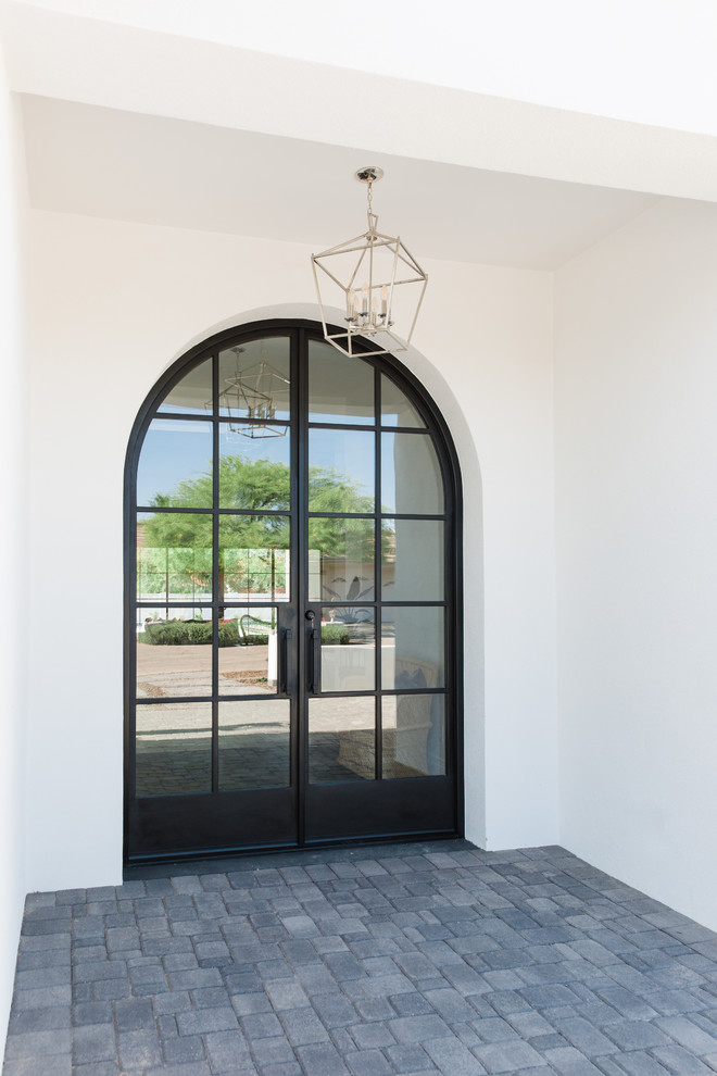Modelo de puerta principal mediterránea grande con paredes blancas, suelo de ladrillo, puerta doble, puerta negra y suelo gris