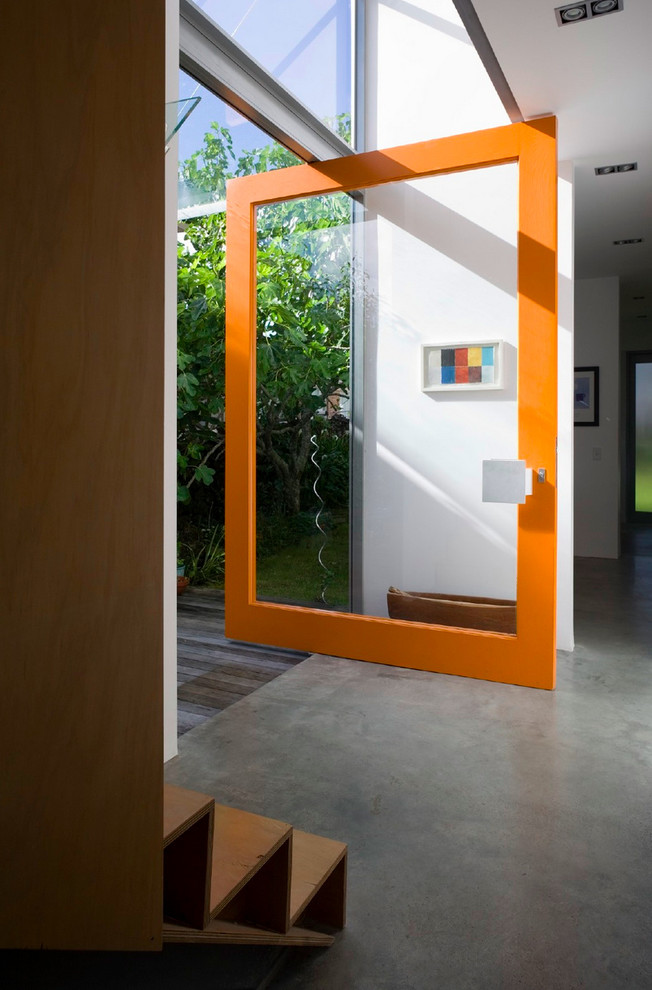 Diseño de entrada contemporánea con paredes blancas, suelo de cemento, puerta pivotante y puerta de vidrio