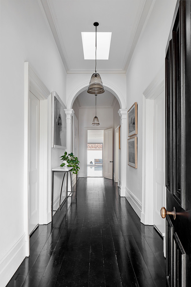 Стильный дизайн: узкая прихожая в современном стиле с белыми стенами, черным полом, деревянным полом, одностворчатой входной дверью и черной входной дверью - последний тренд