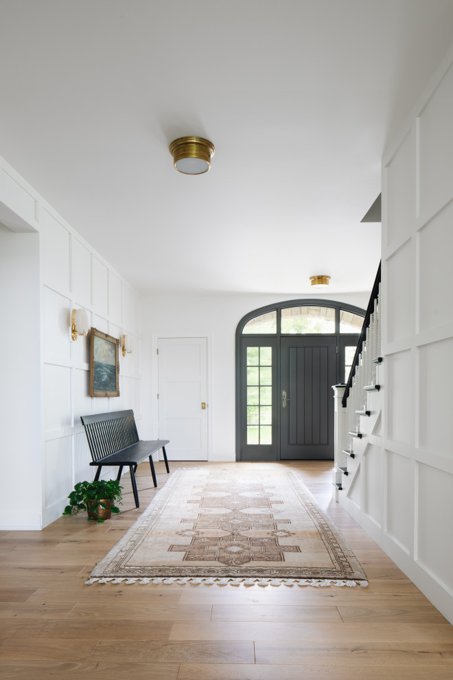 На фото: фойе в стиле неоклассика (современная классика) с белыми стенами, светлым паркетным полом, одностворчатой входной дверью, черной входной дверью и бежевым полом с
