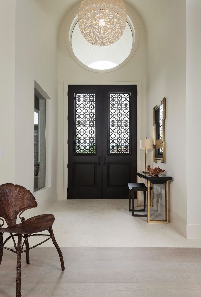 他の地域にある高級な広いトランジショナルスタイルのおしゃれな玄関ロビー (白い壁、ライムストーンの床、白い床、黒いドア) の写真