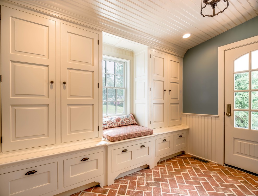 This is an example of a classic boot room in Philadelphia with blue walls, brick flooring, a single front door, a white front door and red floors.