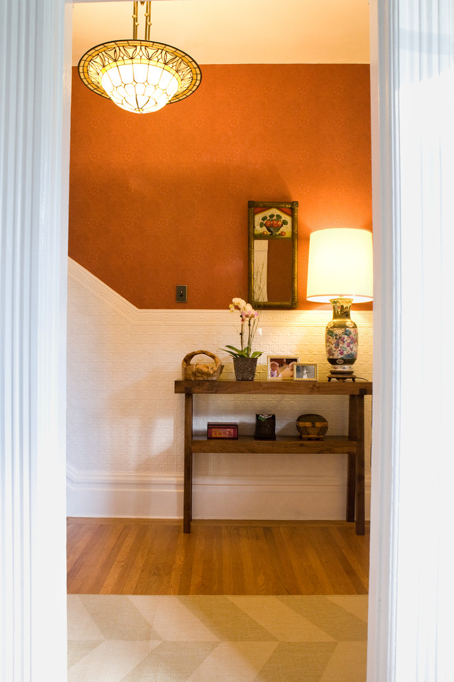 Idée de décoration pour une entrée bohème avec un mur orange et un sol en bois brun.