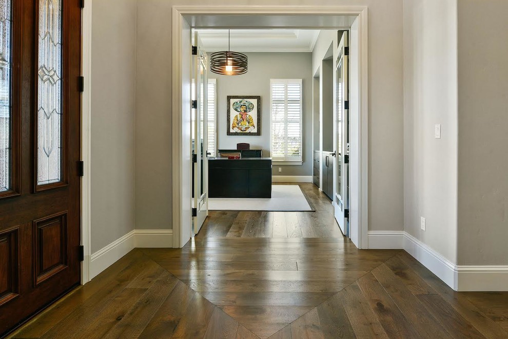 Modelo de puerta principal tradicional renovada de tamaño medio con paredes grises, suelo de madera en tonos medios, puerta simple, puerta de madera en tonos medios y suelo marrón