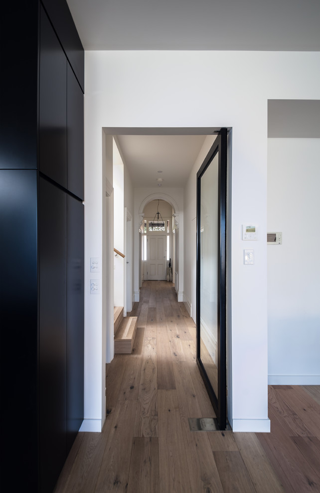 Idee per un piccolo corridoio minimalista con pareti bianche, pavimento in legno massello medio e una porta nera