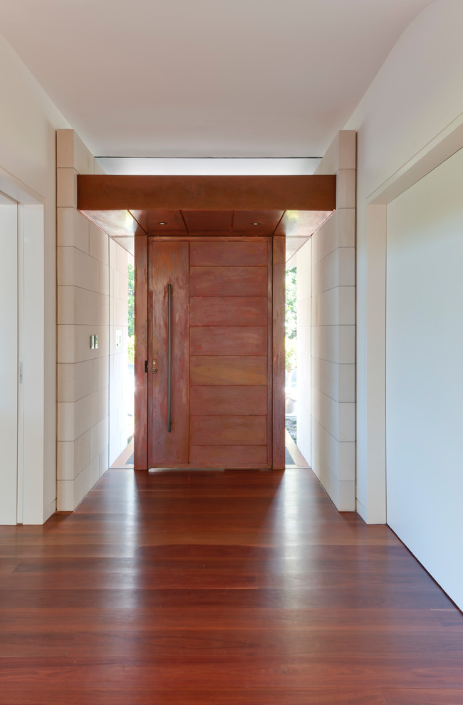 Inspiration pour une entrée minimaliste avec un mur blanc, un sol en bois brun, une porte pivot et une porte en bois brun.
