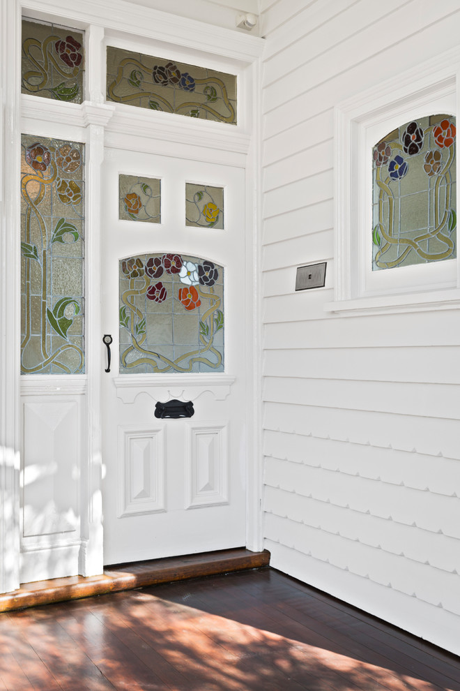 Réalisation d'une porte d'entrée tradition avec un mur blanc, parquet foncé, une porte simple, une porte blanche et un sol marron.