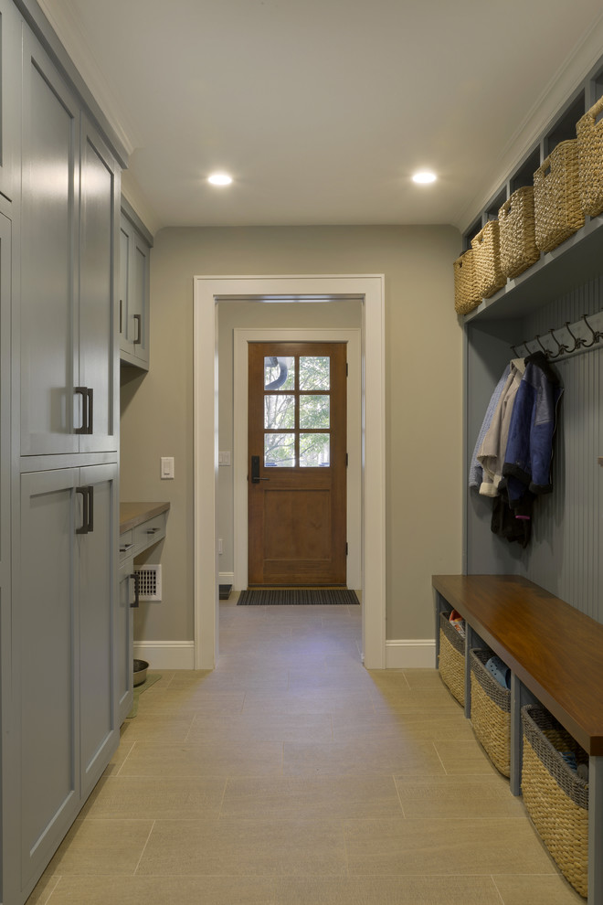 Photo of a large traditional boot room in New York with grey walls, porcelain flooring, a single front door, a medium wood front door and beige floors.