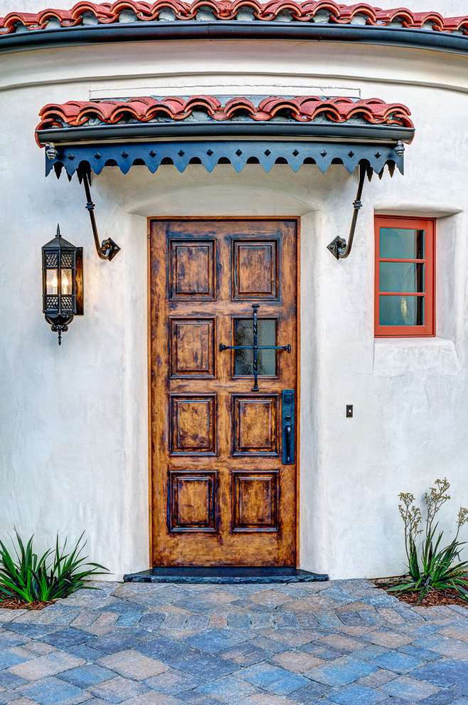 На фото: входная дверь среднего размера в средиземноморском стиле с одностворчатой входной дверью, входной дверью из дерева среднего тона, белыми стенами и разноцветным полом