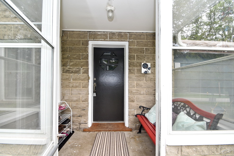 Ejemplo de vestíbulo campestre pequeño con paredes beige, suelo de cemento, puerta simple, puerta negra y suelo gris