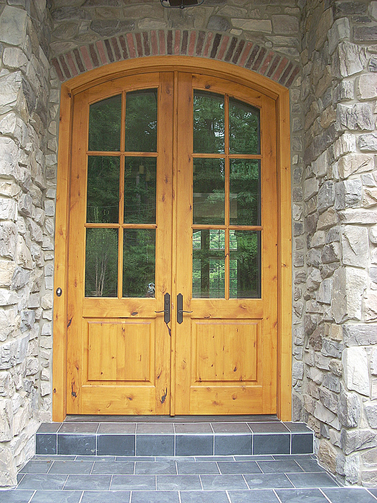 Réalisation d'une grande porte d'entrée chalet avec un mur gris, un sol en ardoise, une porte double et une porte en bois brun.