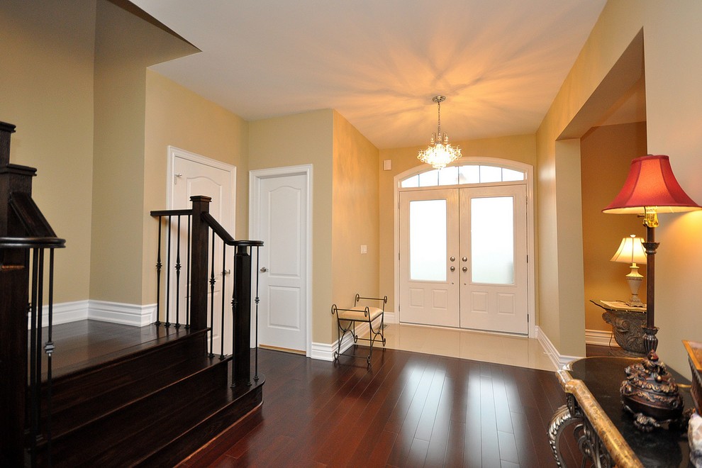 Cette photo montre une entrée chic de taille moyenne avec un couloir, un mur beige, parquet foncé, une porte double, une porte en verre et un sol marron.