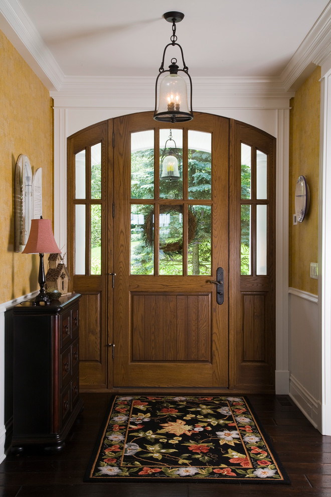 На фото: большая входная дверь: освещение в классическом стиле с желтыми стенами, темным паркетным полом, одностворчатой входной дверью и входной дверью из дерева среднего тона с