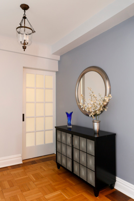 Cette image montre un petit hall d'entrée minimaliste avec un mur gris, un sol en bois brun, une porte simple et une porte noire.