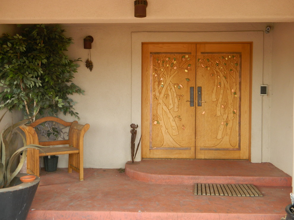 Cette image montre une grande porte d'entrée sud-ouest américain avec un mur blanc, sol en béton ciré, une porte double et une porte en bois brun.