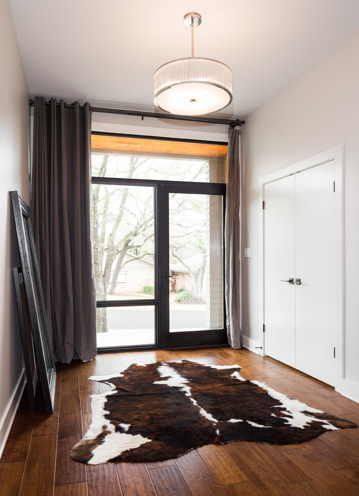 Klassisches Foyer mit grauer Wandfarbe, braunem Holzboden und schwarzer Haustür in Austin