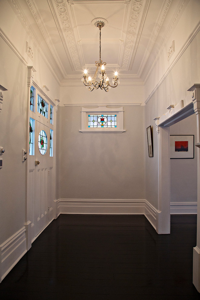 Cette image montre un hall d'entrée traditionnel de taille moyenne avec un mur blanc, parquet foncé, une porte simple, une porte blanche et un sol marron.