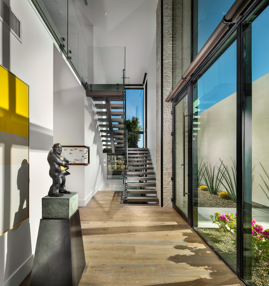 Esempio di un ampio ingresso minimal con pareti bianche, parquet chiaro, una porta a pivot, una porta in vetro e pavimento marrone