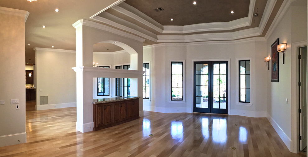Photo of a large mediterranean foyer in New Orleans with light hardwood flooring, grey walls, a double front door, a glass front door and brown floors.