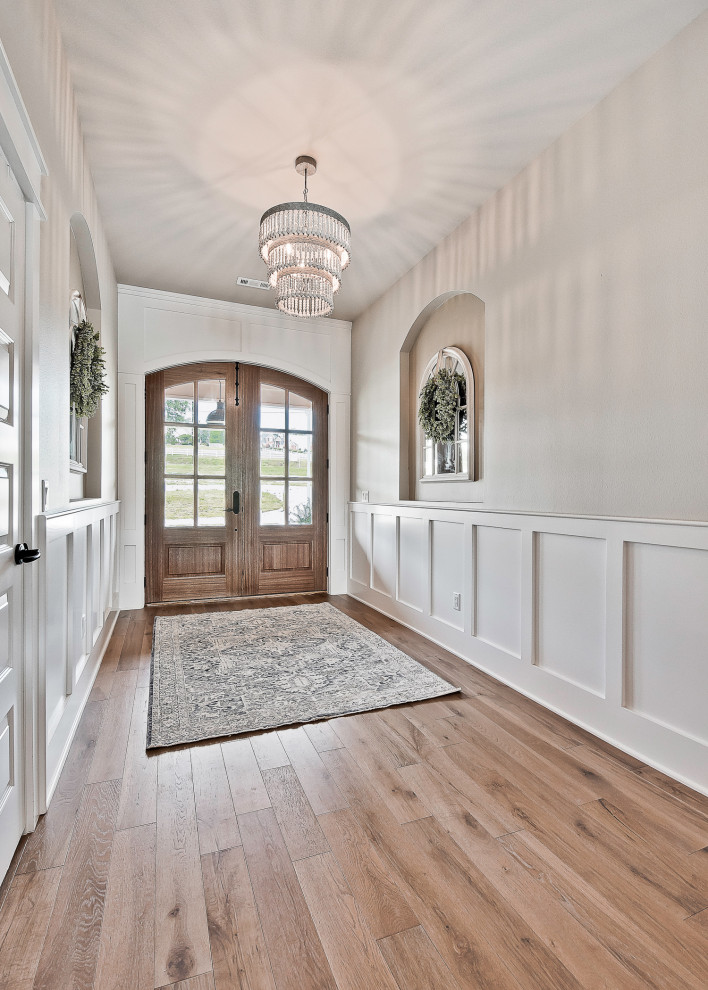 Modelo de entrada de estilo de casa de campo con paredes beige, suelo de madera clara, puerta doble y puerta de madera clara