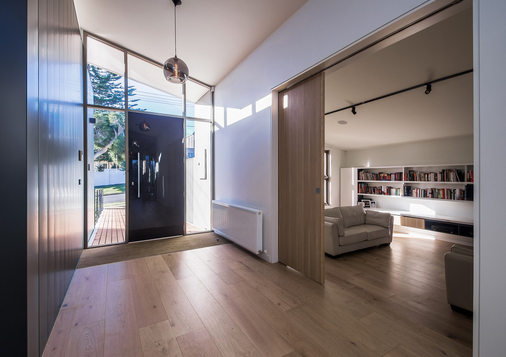 Ejemplo de distribuidor minimalista de tamaño medio con paredes blancas, suelo de madera en tonos medios, puerta simple, puerta gris y suelo marrón