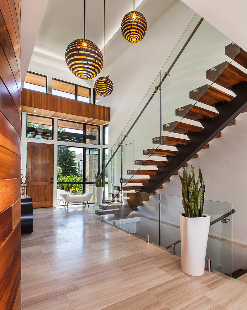 This is an example of a contemporary foyer in Detroit with white walls, a single front door, a medium wood front door, brown floors and feature lighting.