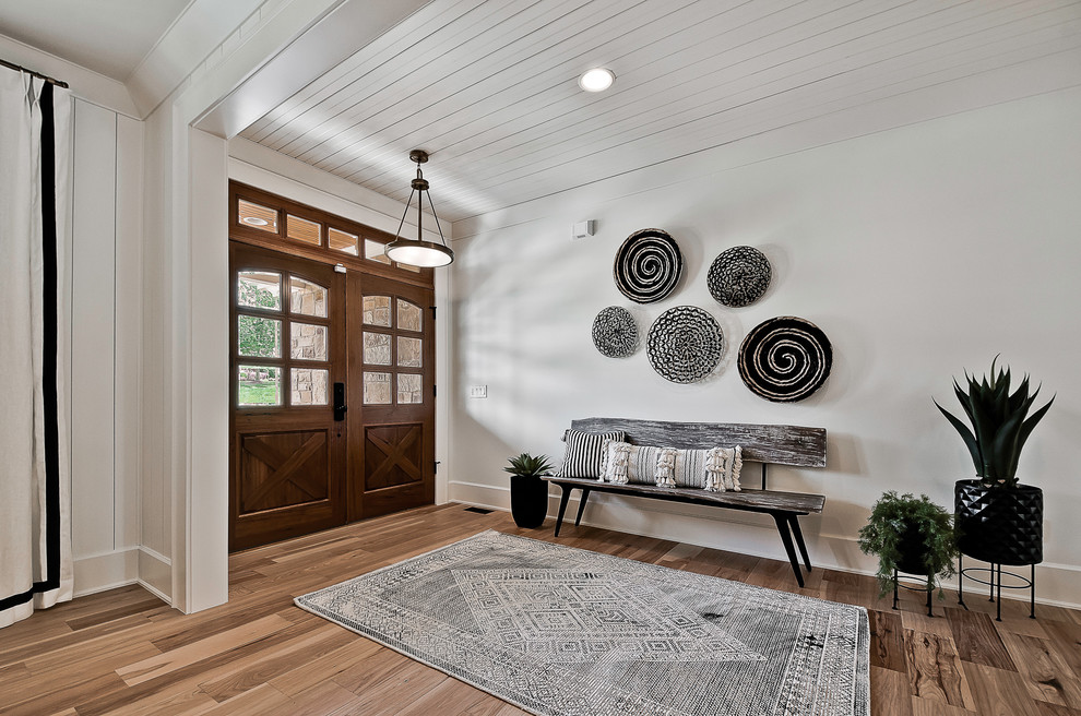 Diseño de hall campestre con paredes blancas, suelo de madera en tonos medios, puerta doble, puerta de madera oscura y suelo marrón