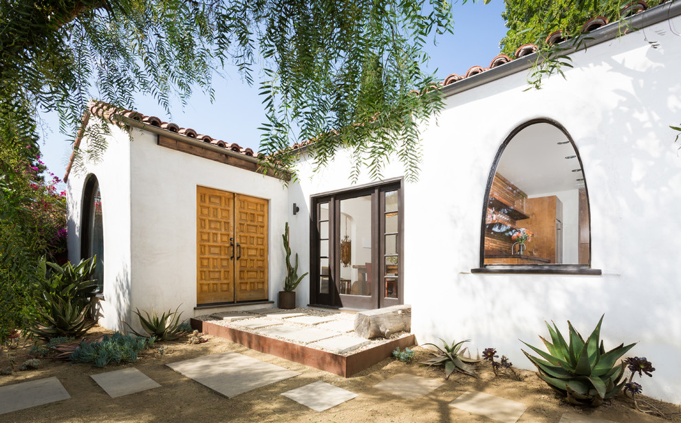 Kleine Mediterrane Haustür mit Doppeltür, hellbrauner Holzhaustür, weißer Wandfarbe, Betonboden und grauem Boden in Los Angeles