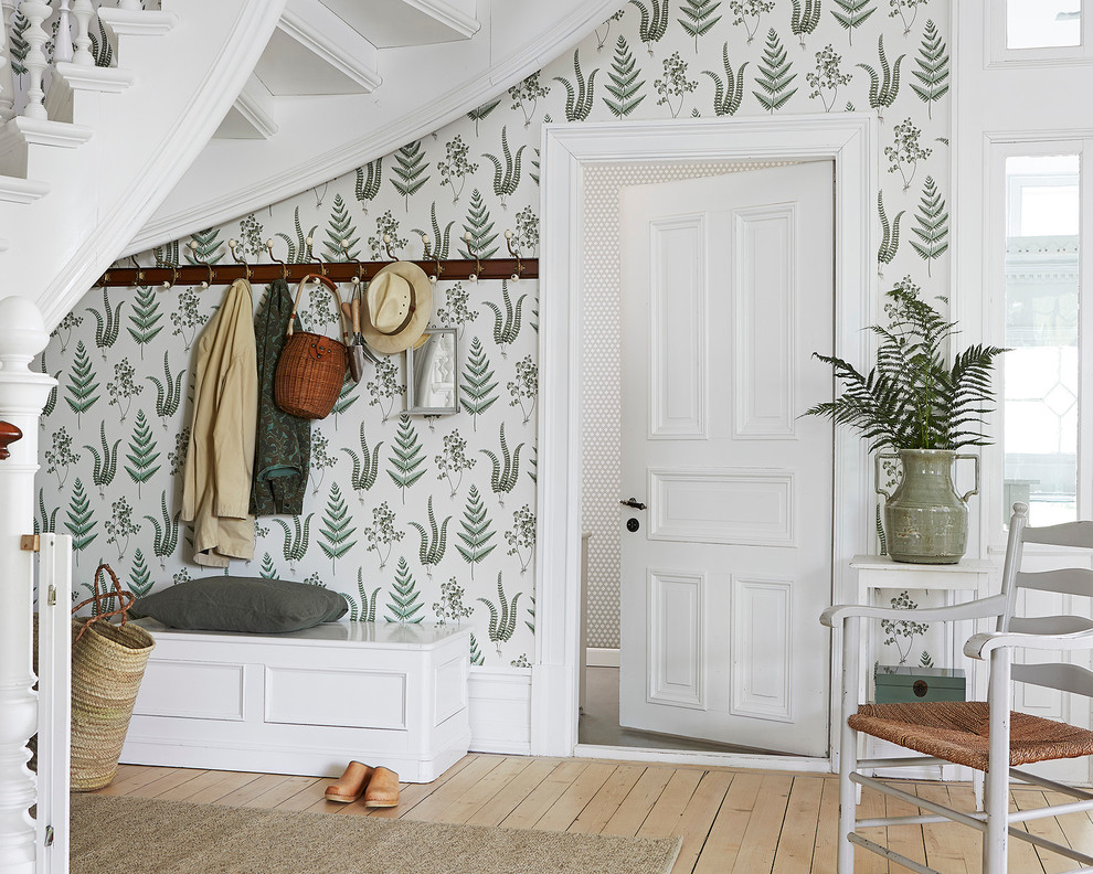 Inredning av ett lantligt mellanstort kapprum, med gröna väggar, ljust trägolv, en enkeldörr och en vit dörr