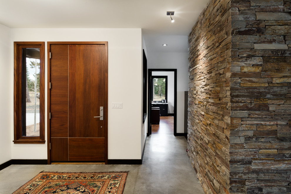 Cette image montre un grand hall d'entrée design avec un mur blanc, sol en béton ciré, une porte simple, une porte en bois brun et un sol gris.