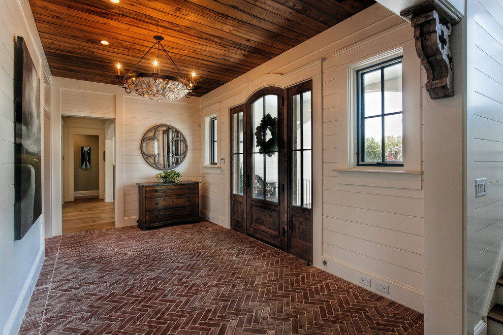 Cette photo montre un vestibule chic avec un mur blanc, un sol en brique, une porte simple et une porte en bois foncé.