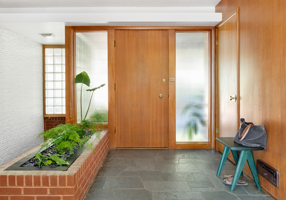 Cette photo montre un hall d'entrée rétro de taille moyenne avec un mur blanc, un sol en ardoise, une porte simple, une porte en bois brun et un sol vert.