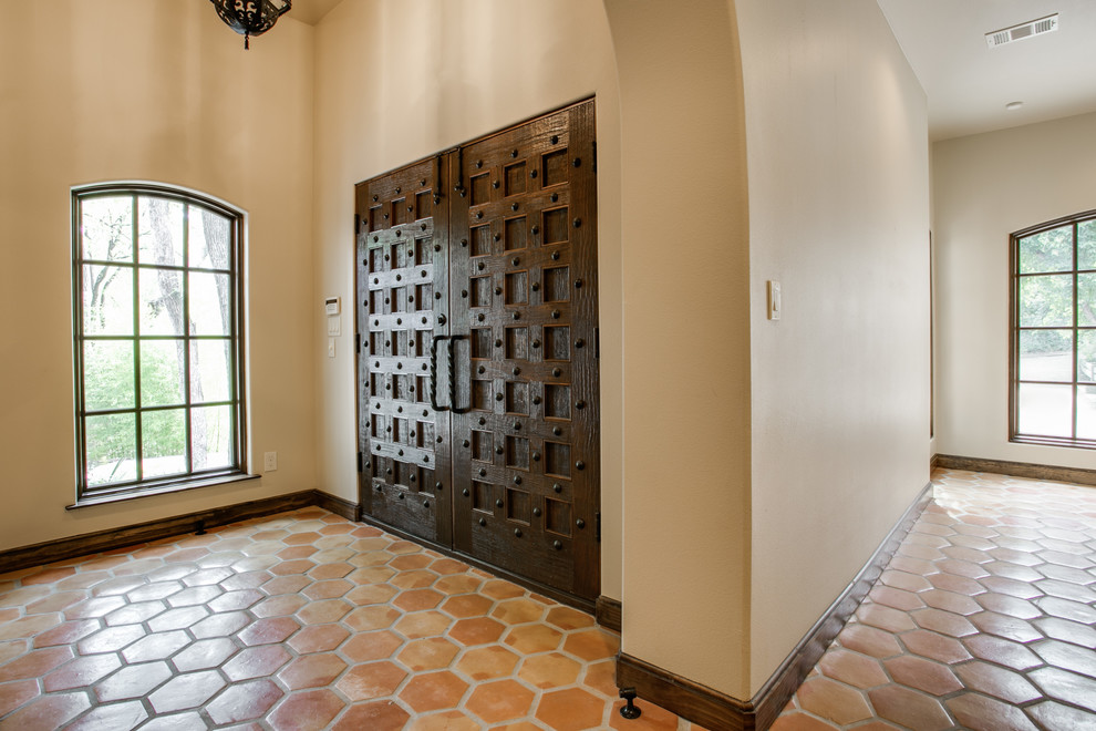 ダラスにあるラグジュアリーな広い地中海スタイルのおしゃれな玄関ドア (ベージュの壁、テラコッタタイルの床、濃色木目調のドア) の写真