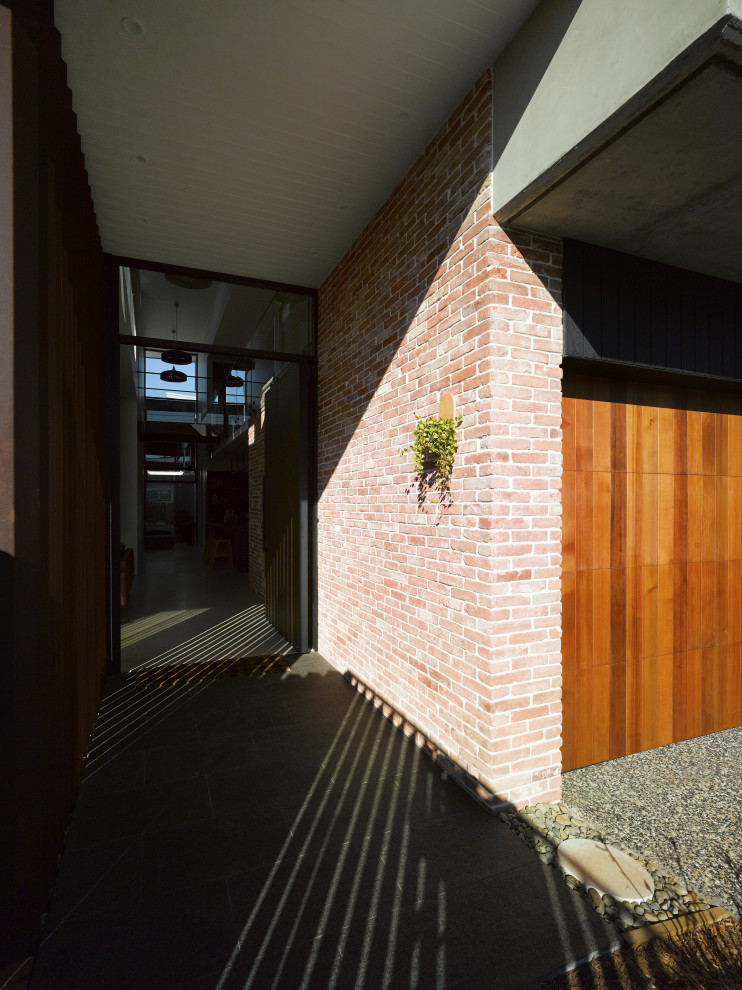 Diseño de puerta principal industrial de tamaño medio con paredes rojas, suelo de granito, puerta pivotante, puerta de vidrio, suelo negro y ladrillo