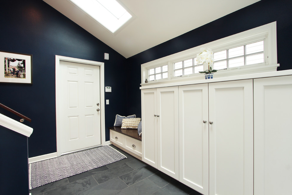 Cette image montre une grande entrée traditionnelle avec un vestiaire, un mur bleu, un sol en ardoise, une porte simple, un sol gris et une porte blanche.
