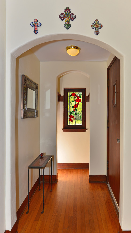 Modelo de hall mediterráneo pequeño con paredes blancas, suelo de madera en tonos medios, puerta pivotante y puerta de madera en tonos medios