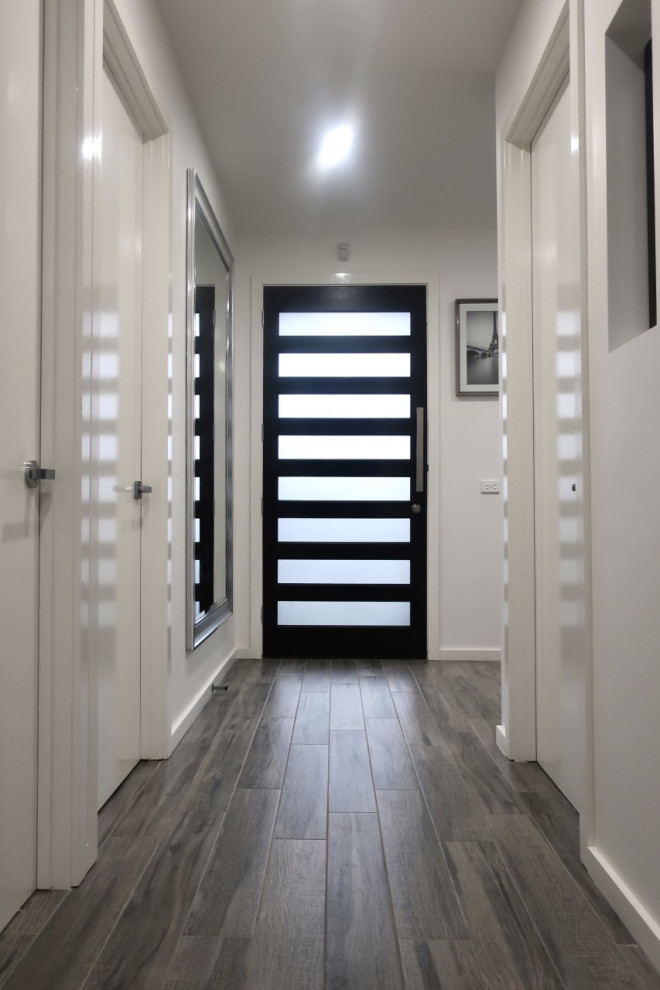 Idee per un corridoio moderno di medie dimensioni con pareti bianche, pavimento con piastrelle in ceramica, una porta singola, una porta in legno scuro e pavimento grigio