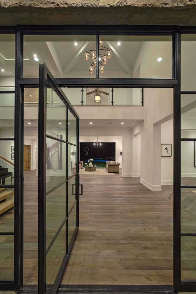 Aménagement d'un grand hall d'entrée contemporain avec un mur blanc, un sol en bois brun, une porte simple et une porte en verre.