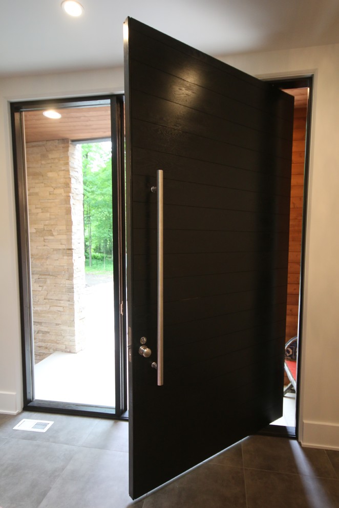 Imagen de puerta principal contemporánea extra grande con paredes blancas, suelo de baldosas de porcelana, puerta pivotante, puerta de madera oscura y suelo gris