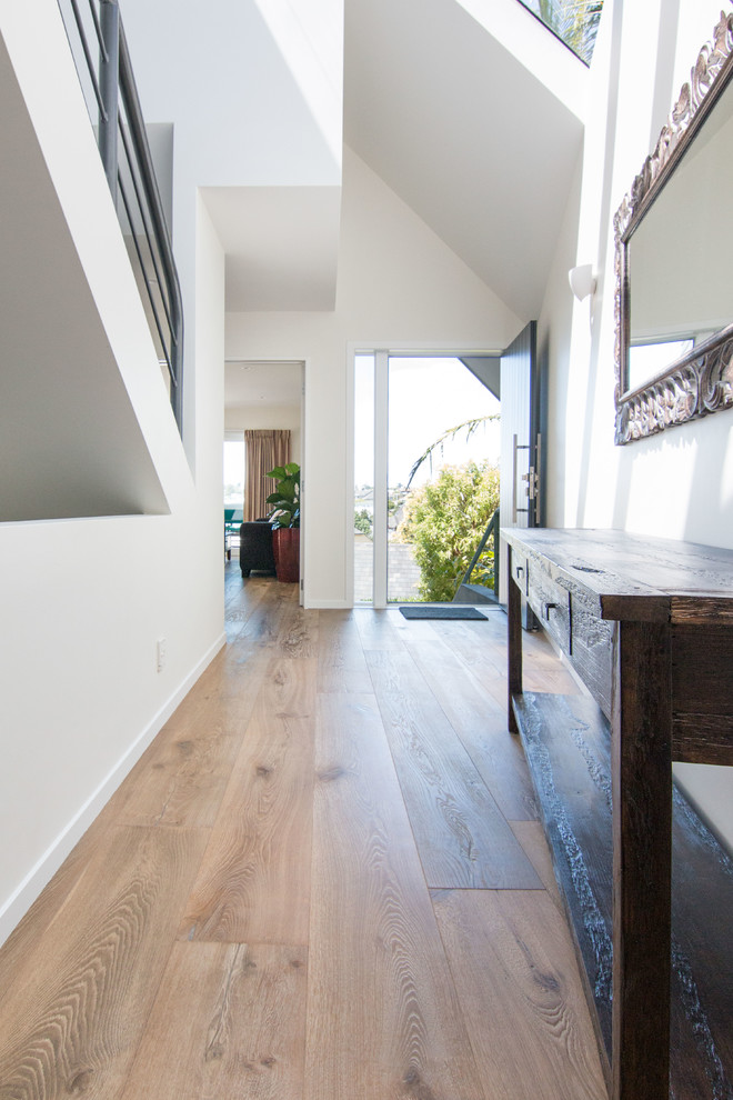 Example of a mid-sized trendy medium tone wood floor and beige floor entryway design in Auckland with white walls and a black front door