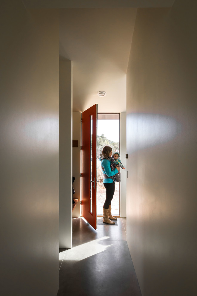 Cette image montre une petite porte d'entrée design avec sol en béton ciré, une porte simple et une porte orange.